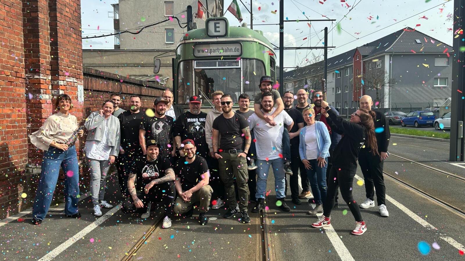 Eine feiernde Menschengruppe vor einer historischen Straßenbahn.