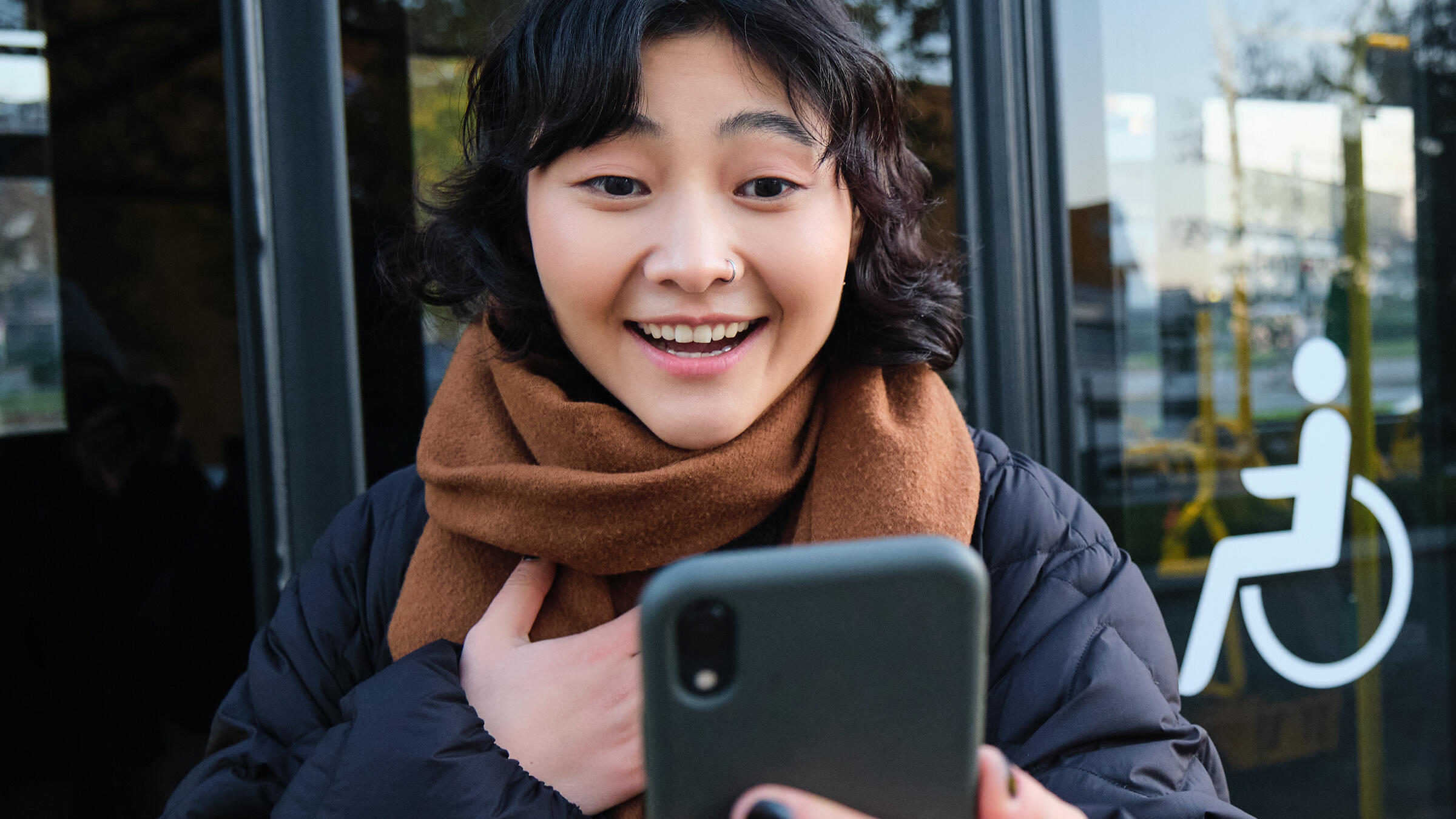 Enthusiastische Frau an einer Bushaltestelle schaut auf ihr Smartphone.