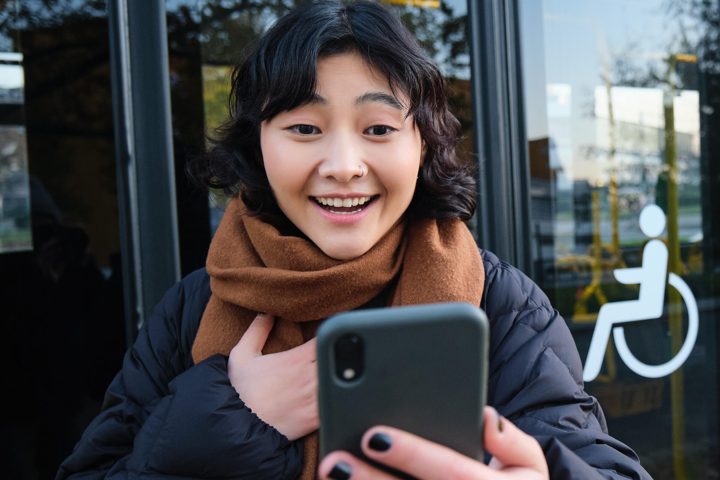 Enthusiastische Frau an einer Bushaltestelle schaut auf ihr Smartphone.