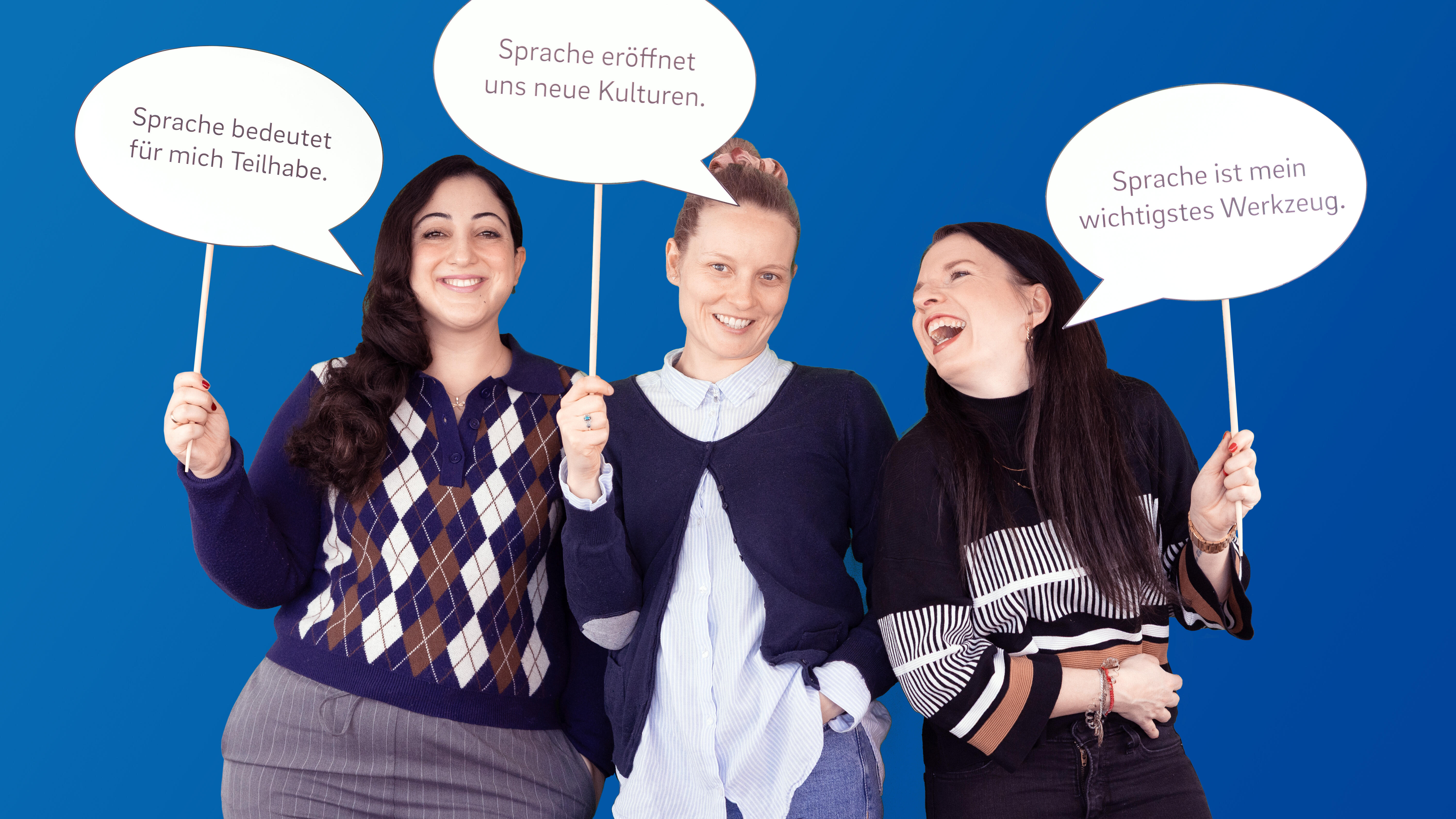 Drei fröhliche Mitarbeitende der VDV-Akademie halten Schilder hoch, auf denen Vorteile von Sprache im Berufskontext stehen.