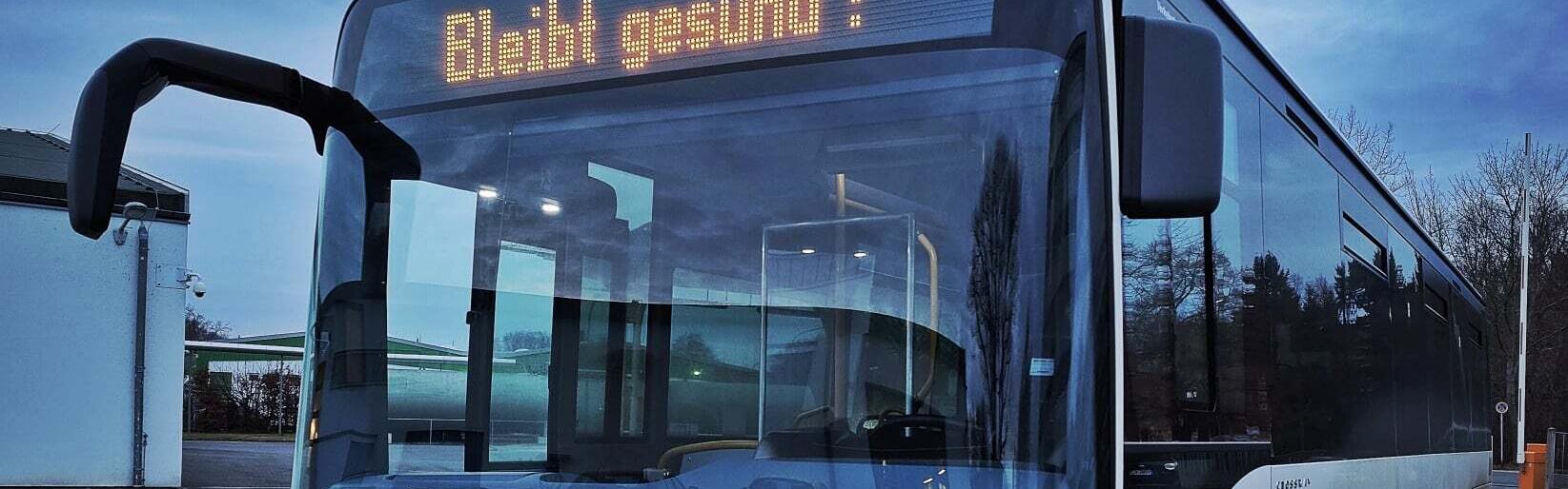 Die Außenanzeige im Fronfenster eines weißen Busses zeigt an: Bleib gesund!