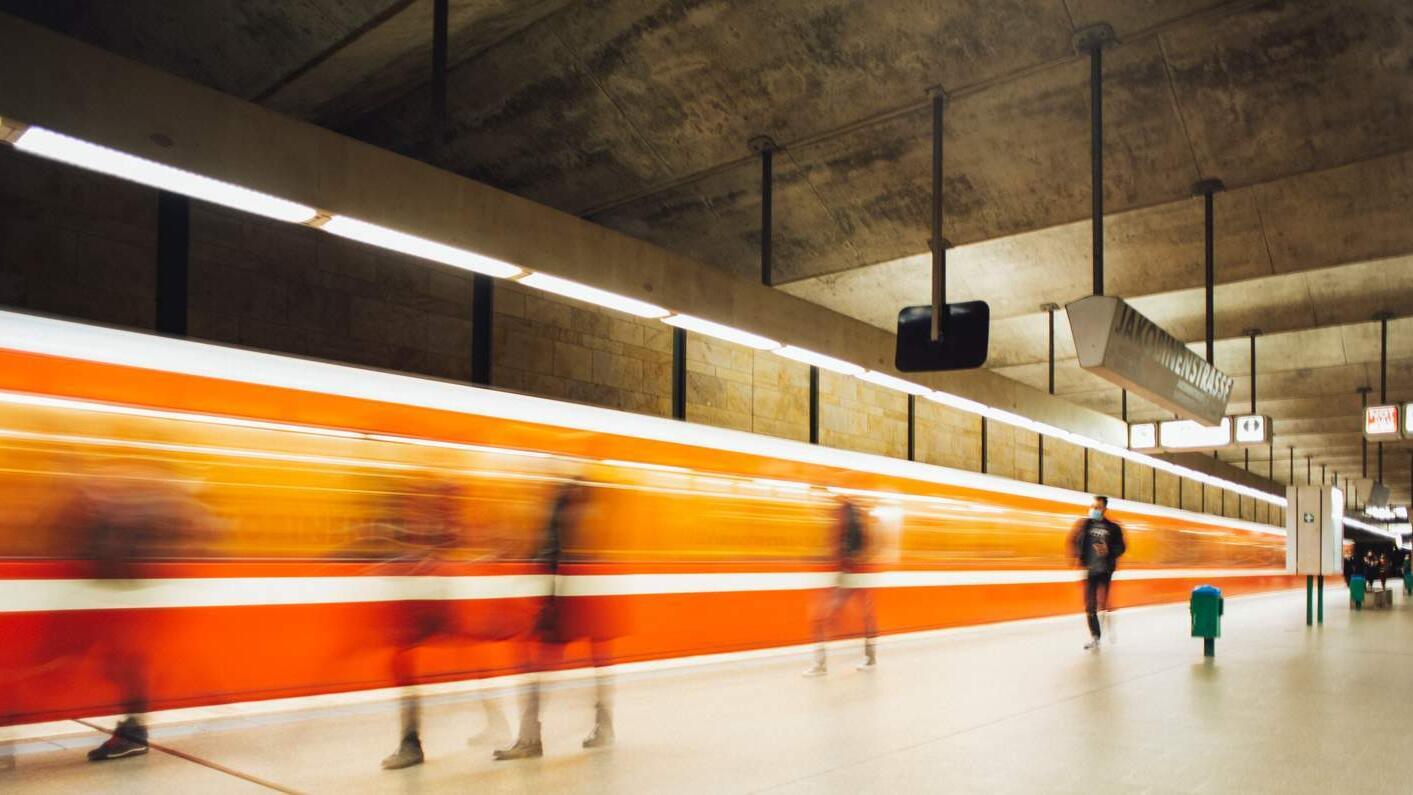 Bahnsteig mit Menschen und einer fahrenden Bahn in Bewegung und Unschärfe