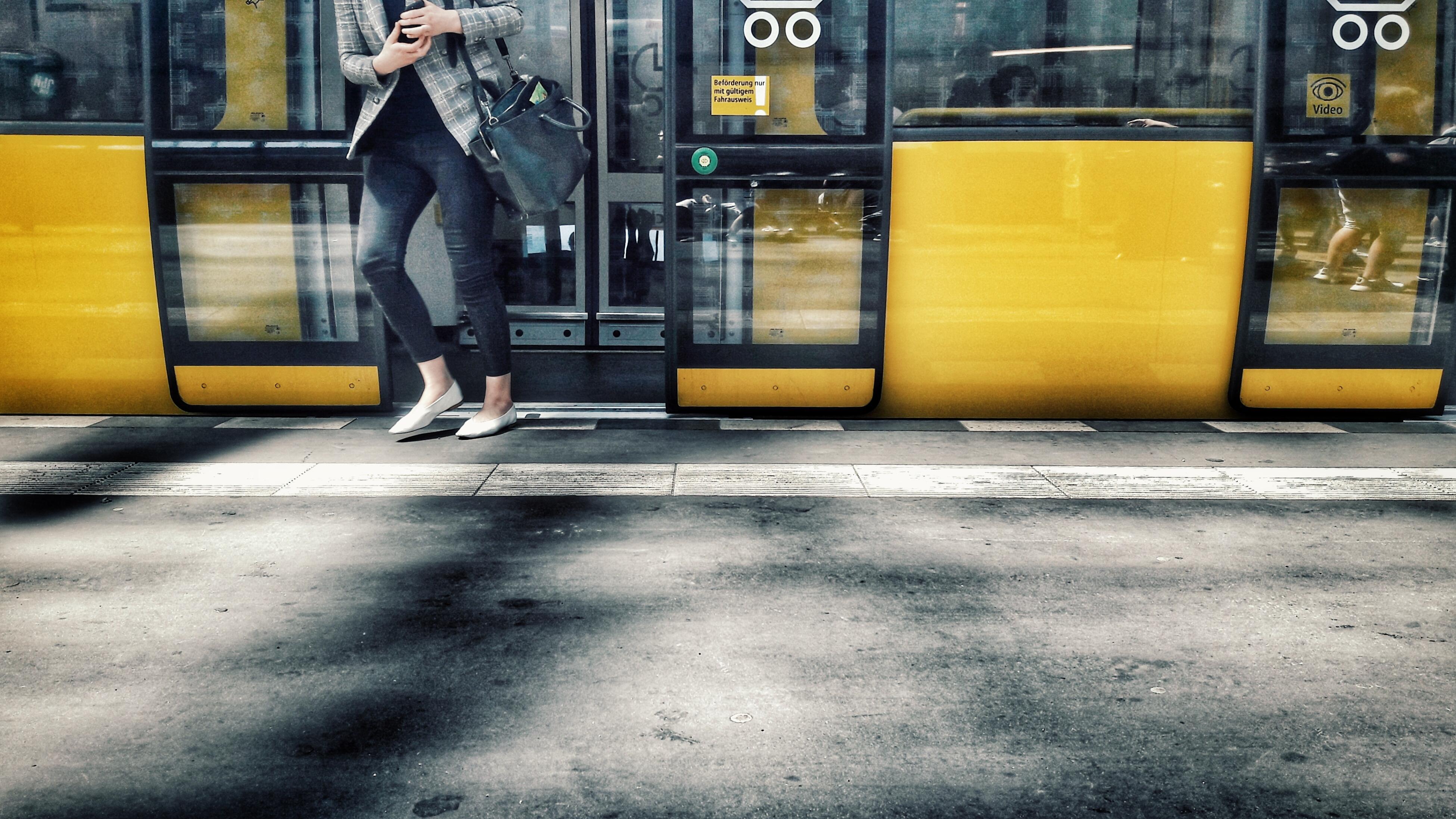 Gelbe Straßenbahn im Hintergrund, davor sieht man eine Frau von den Schultern abwärts, die aussteigt