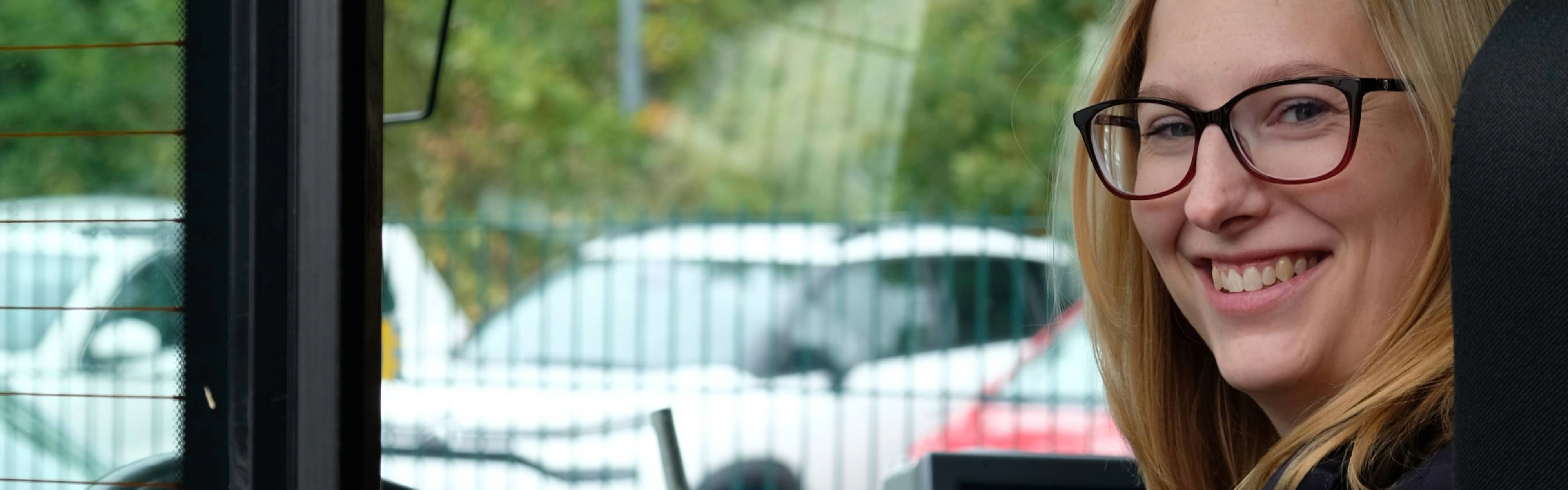 Eine Busfahrerin sitzt im Bus und schaut über ihre Schulter hinaus