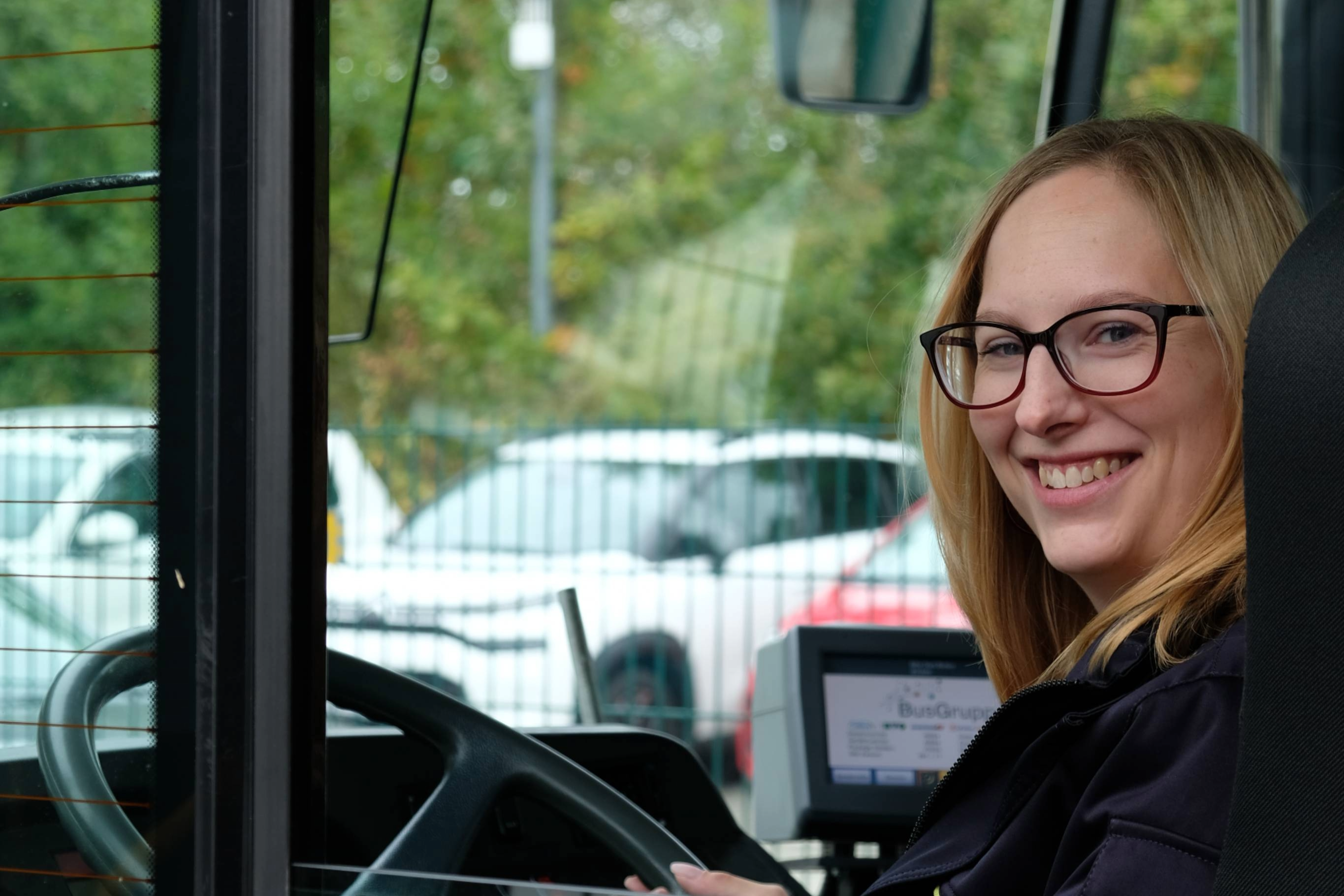 Eine Busfahrerin sitzt im Bus und schaut über ihre Schulter hinaus