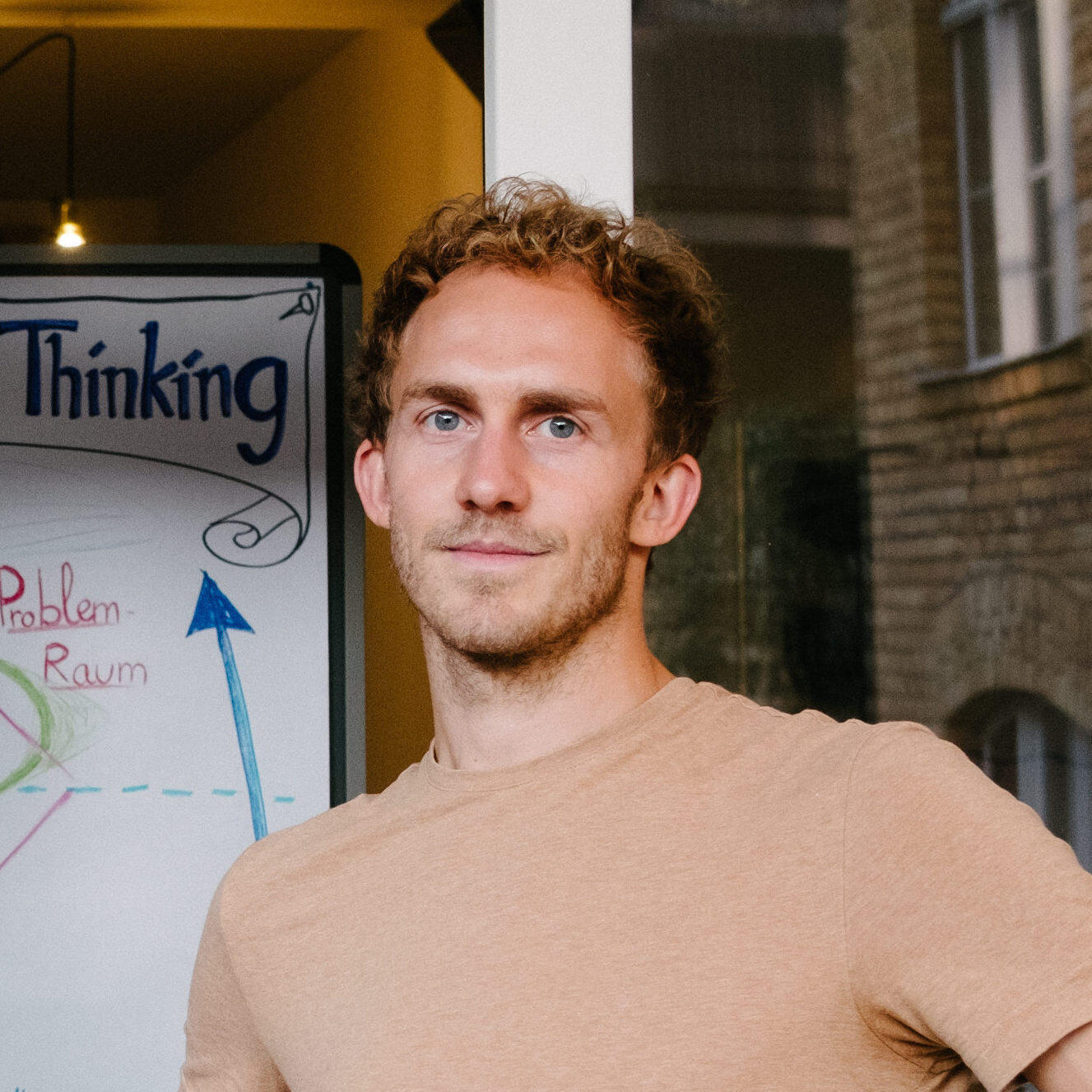 Der Dozent Karl Hosang ist zu sehen. Er lächelt in die Kamera. Er hat kurze dunkelnlode Haare und einen beigen Pullover an.