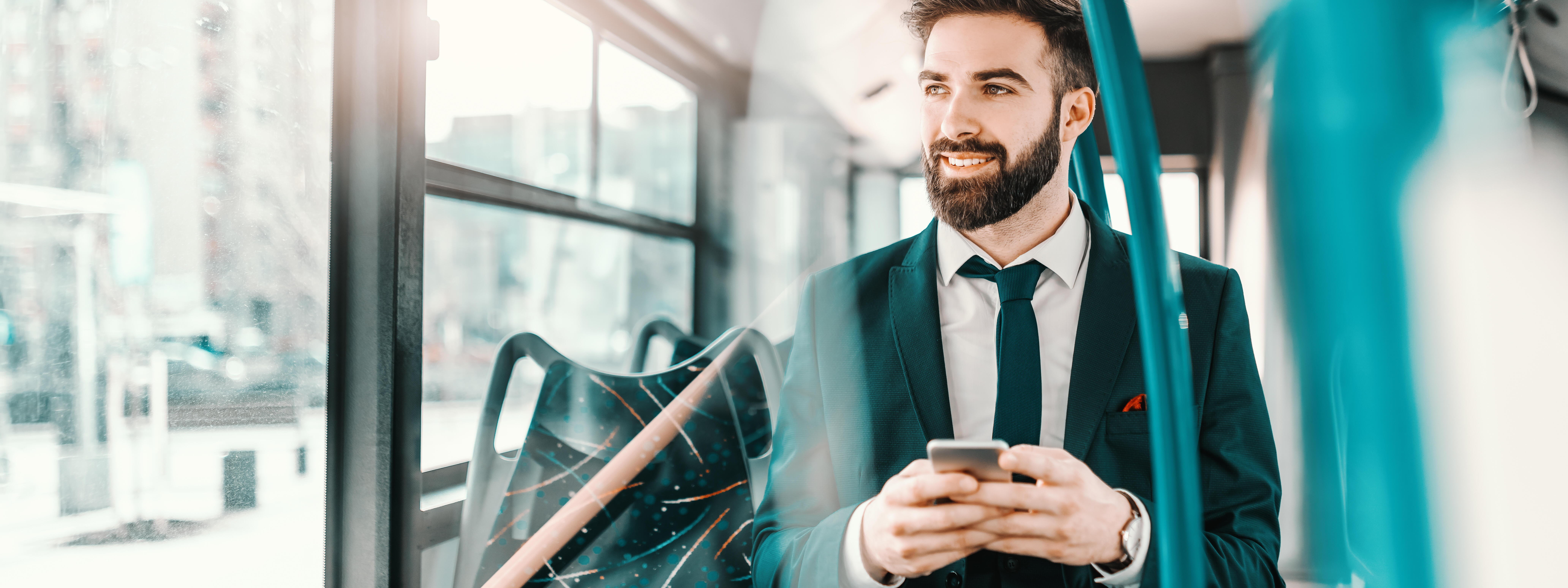 Smiling bearded Caucasian businessman in formal wear sitting in public transport and using smart phone.