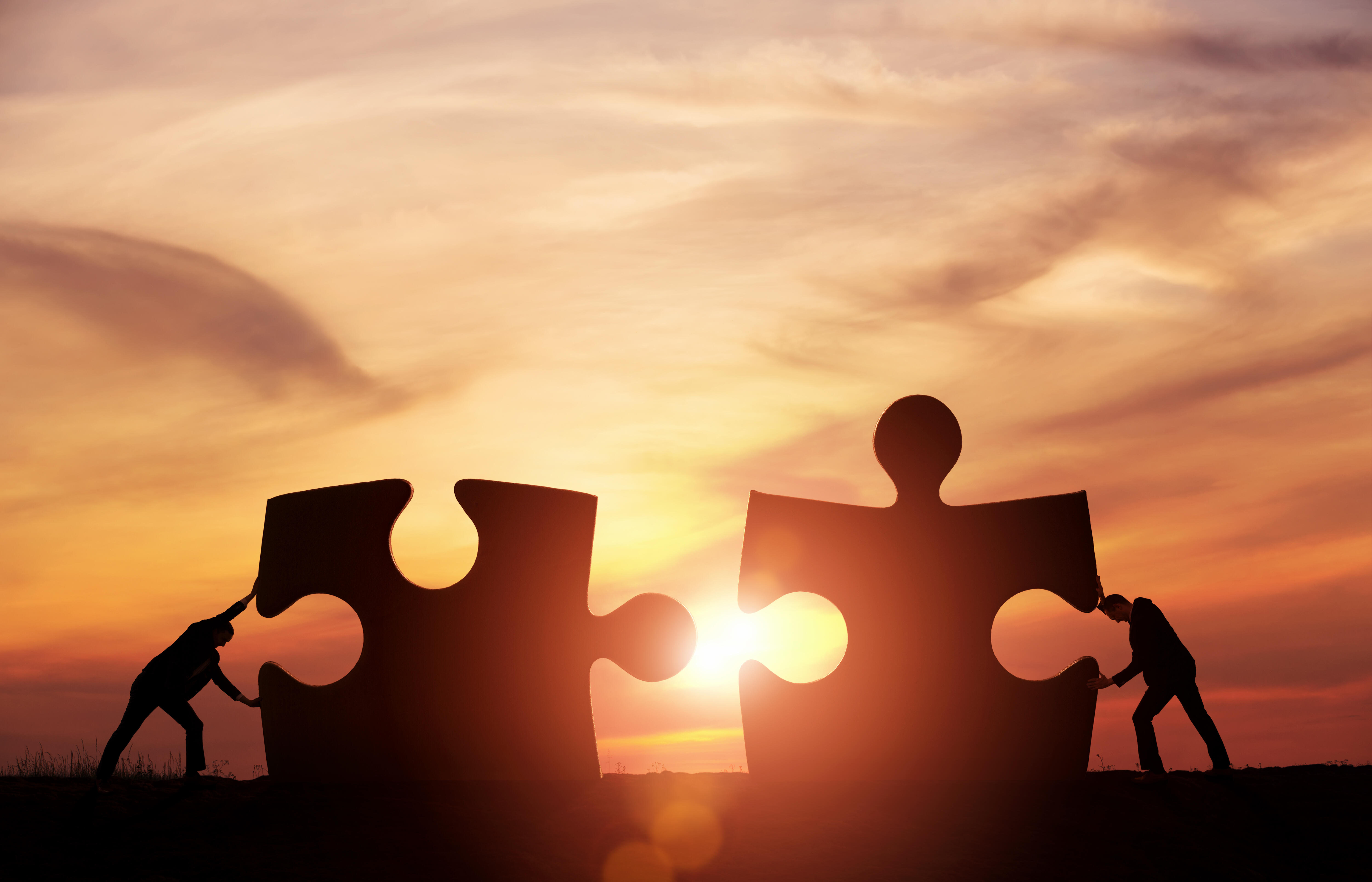 Zwei Personen fügen Puzzleteile zusammen, als Symbol der Zusammenarbeit.