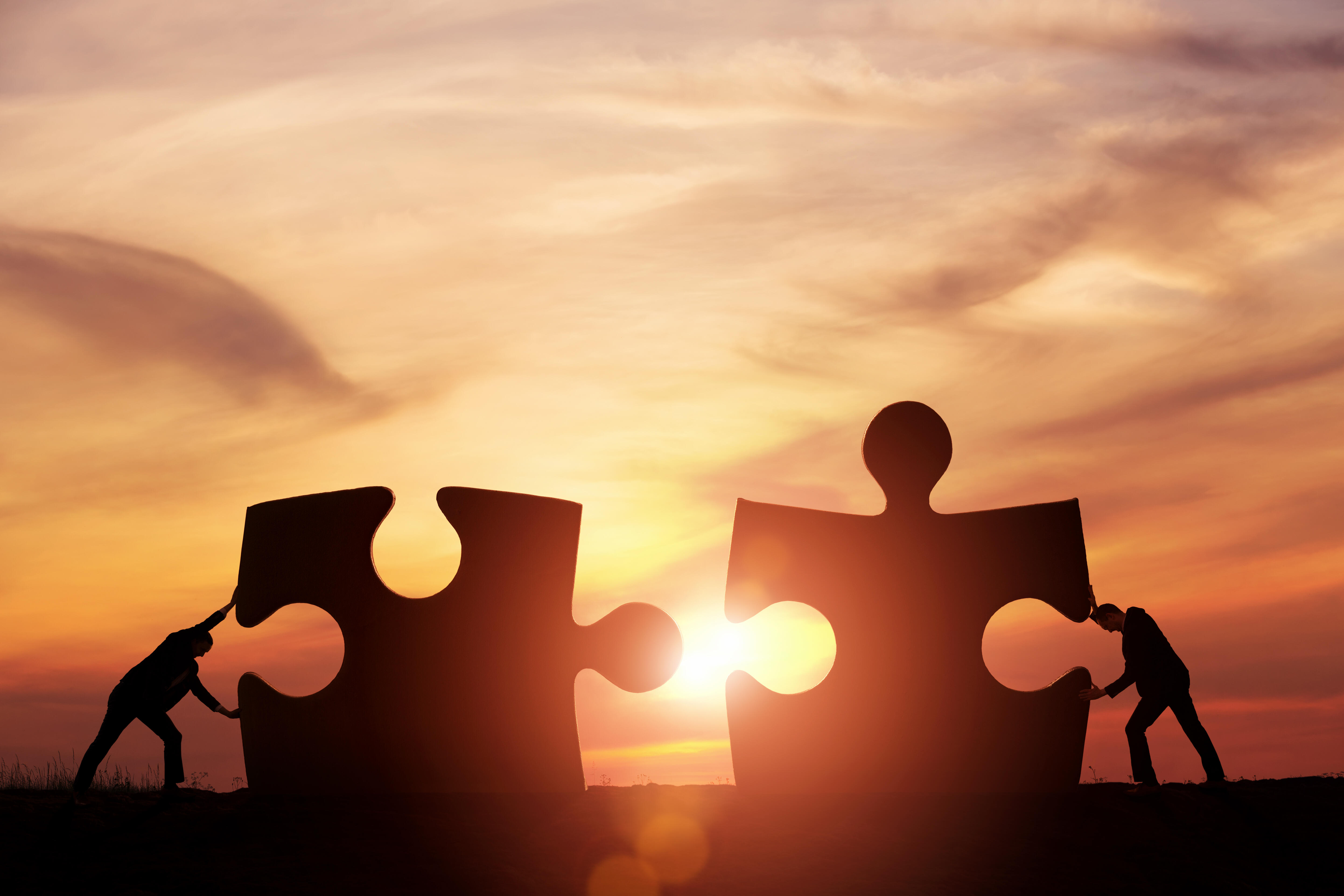 Zwei Personen fügen Puzzleteile zusammen, als Symbol der Zusammenarbeit.