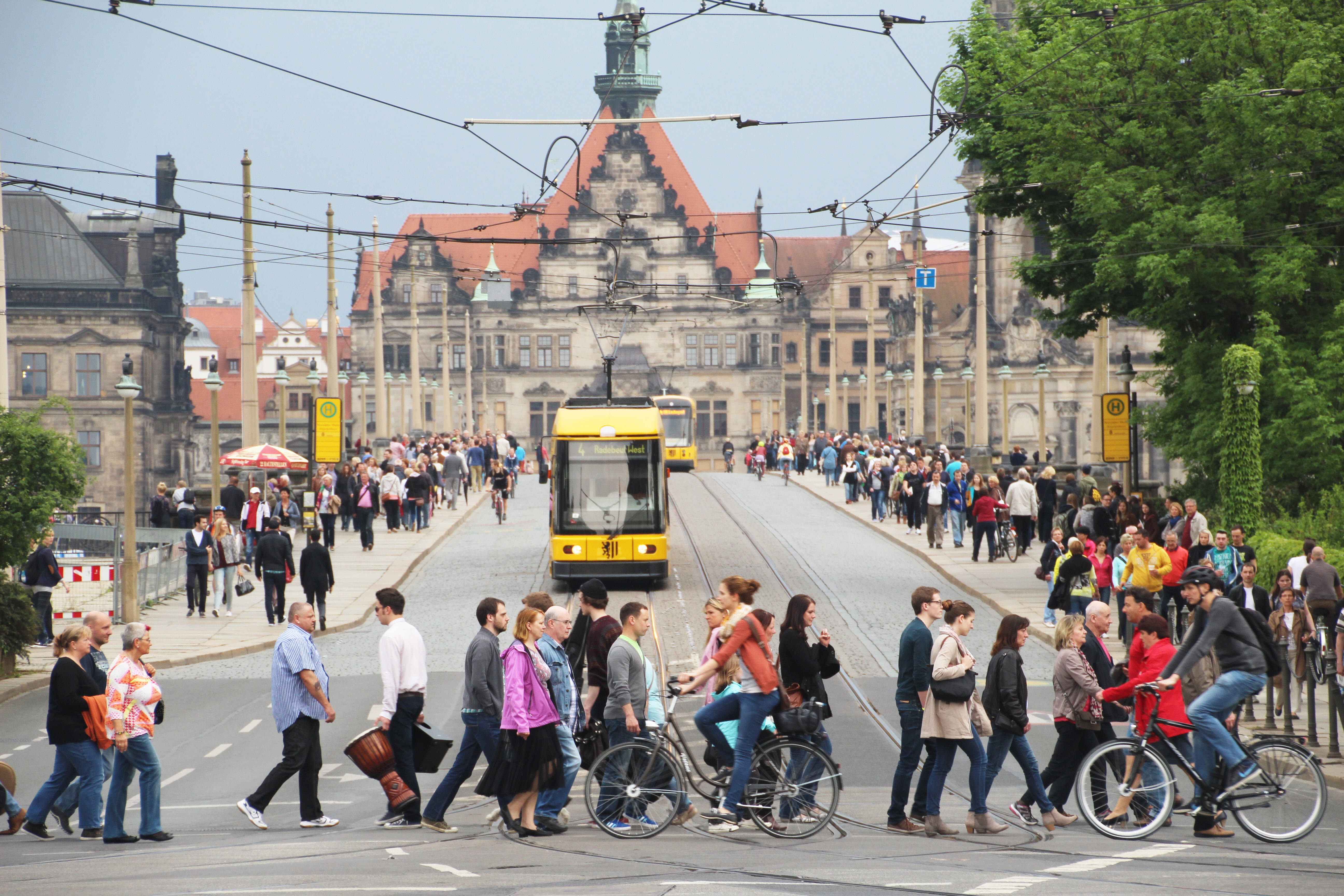 Eine Straßenbahn der Dresdener Verkehrsbetriebe fährt über die Augustusbrücke. Im Vordergrund überqueren viele Passanten die Strecke.