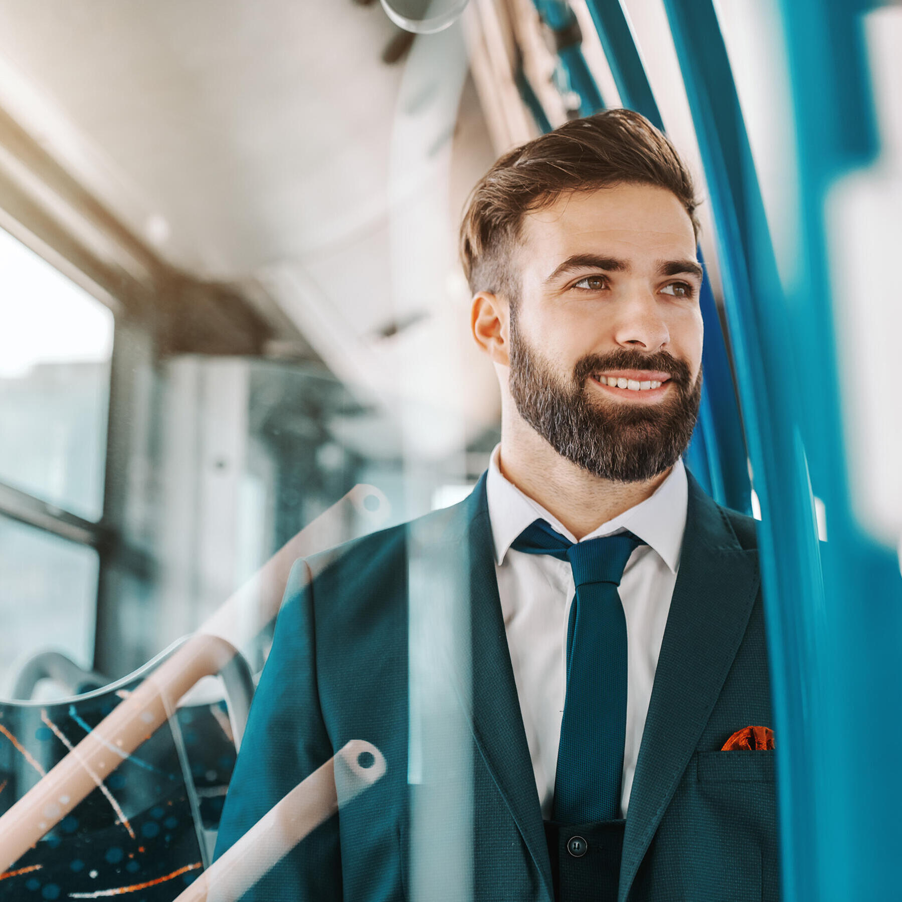 Nahaufnahme eines lächelnden bärtigen Geschäftsmannes in formeller Kleidung, der in einem öffentlichen Verkehrsmittel sitzt und aus dem Fenster schaut.