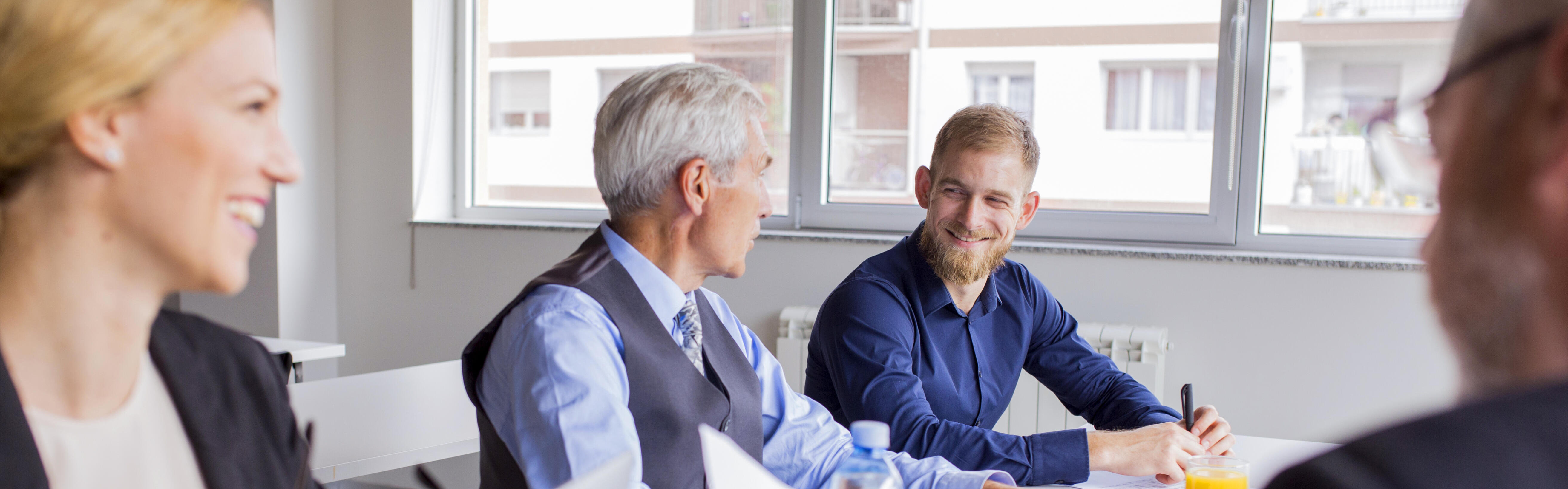 Vier Personen in Business-Dress sitzen mit guter Laune an einem Tisch und arbeiten zusammen.
