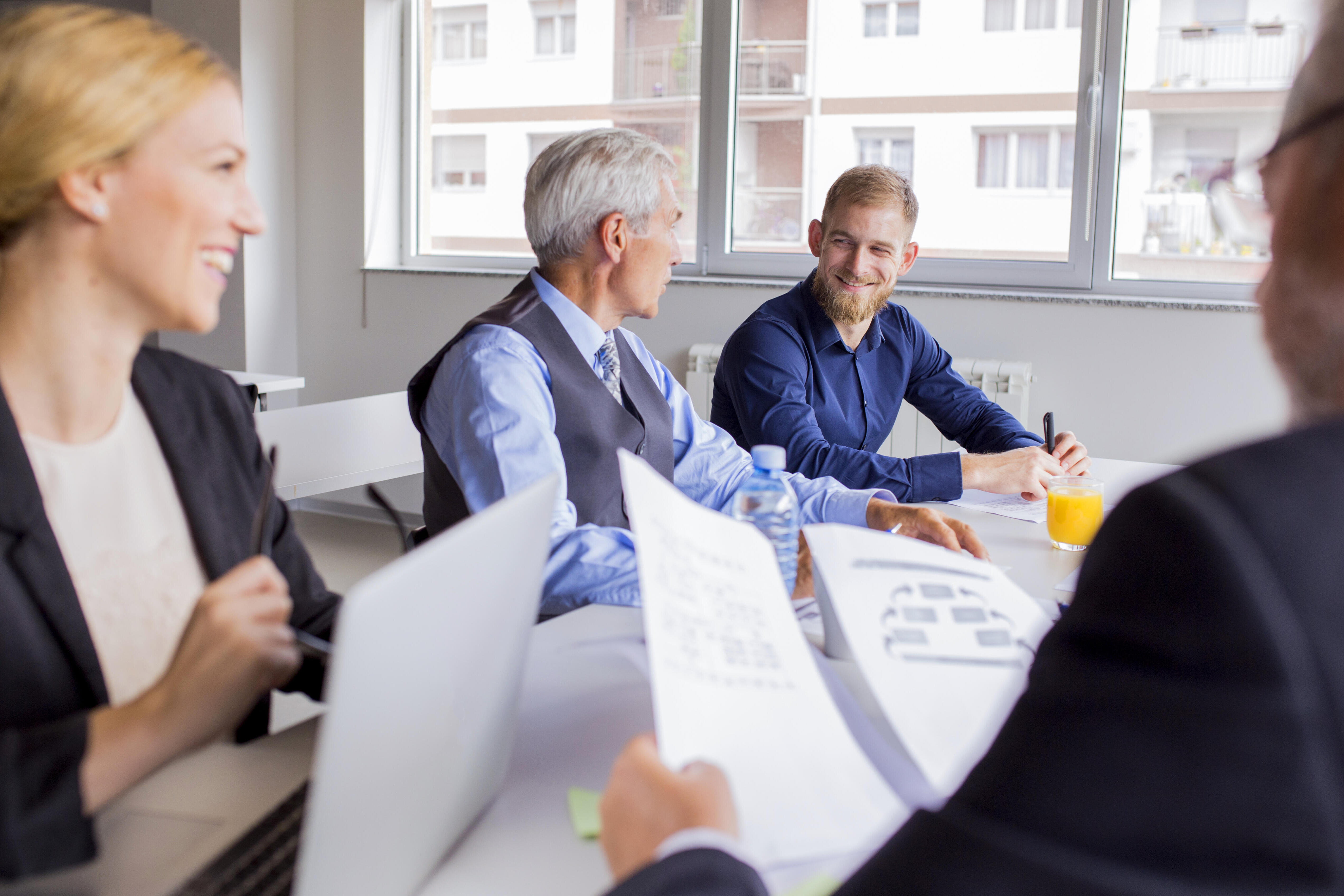 Vier Personen in Business-Dress sitzen mit guter Laune an einem Tisch und arbeiten zusammen.