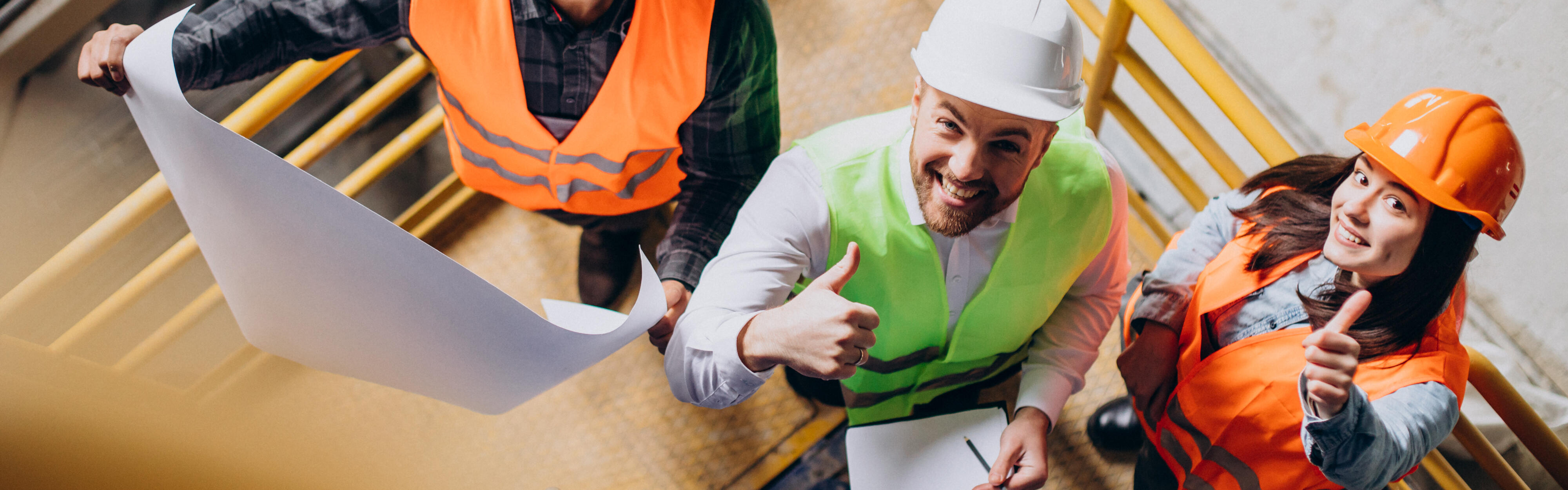 Zwei Bauarbeitende und ein Ingenieur mit Schutzhelmen besprechen den Fertigungsplan.