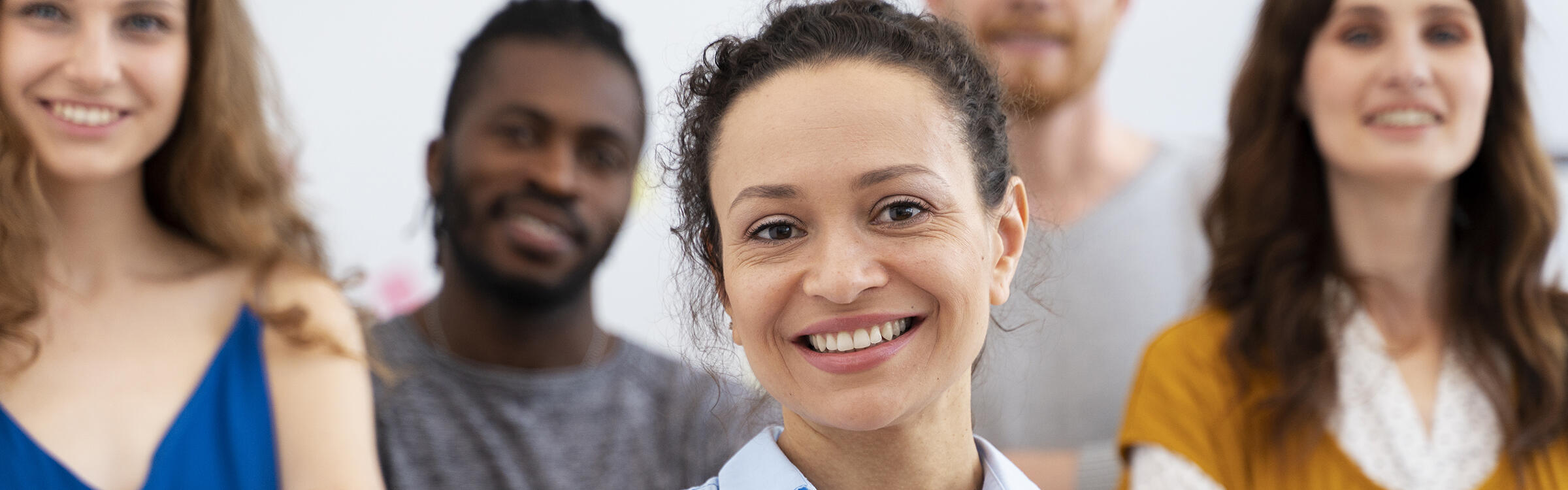 Mehrere Menschen (zwischen 30 und 40), 3 Frauen und 2 Männern, mit unterschiedlicher Hautfarbe schauen lächelnd mit gekreuzten Armen in die Kamera.