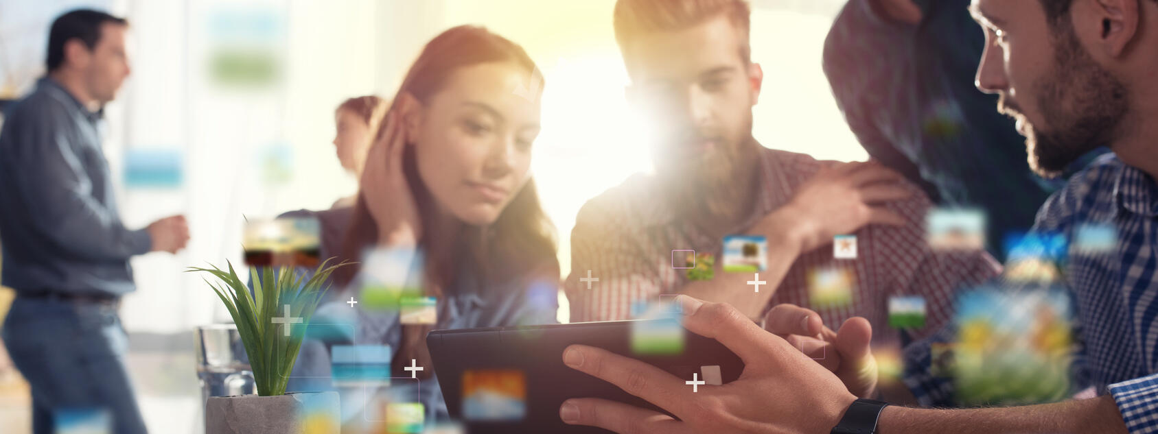 Eine Gruppe von Personen sitzt an einem Tisch und guckt auf ein Tablet.
