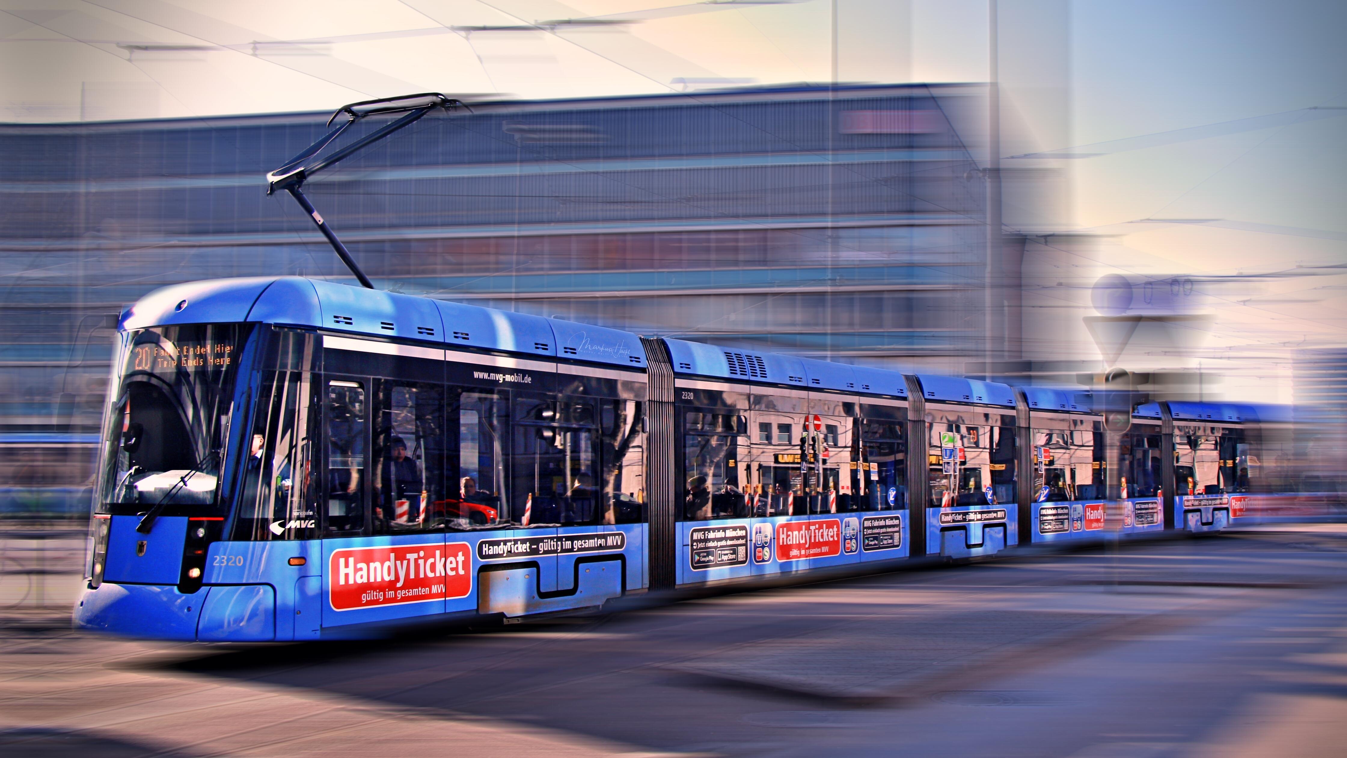 Moderne blaue Straßenbahn der Münchner Verkehrsgesellschaft fährt durch das Stadtgebiet, Hintergrund unscharf durch Bewegung.