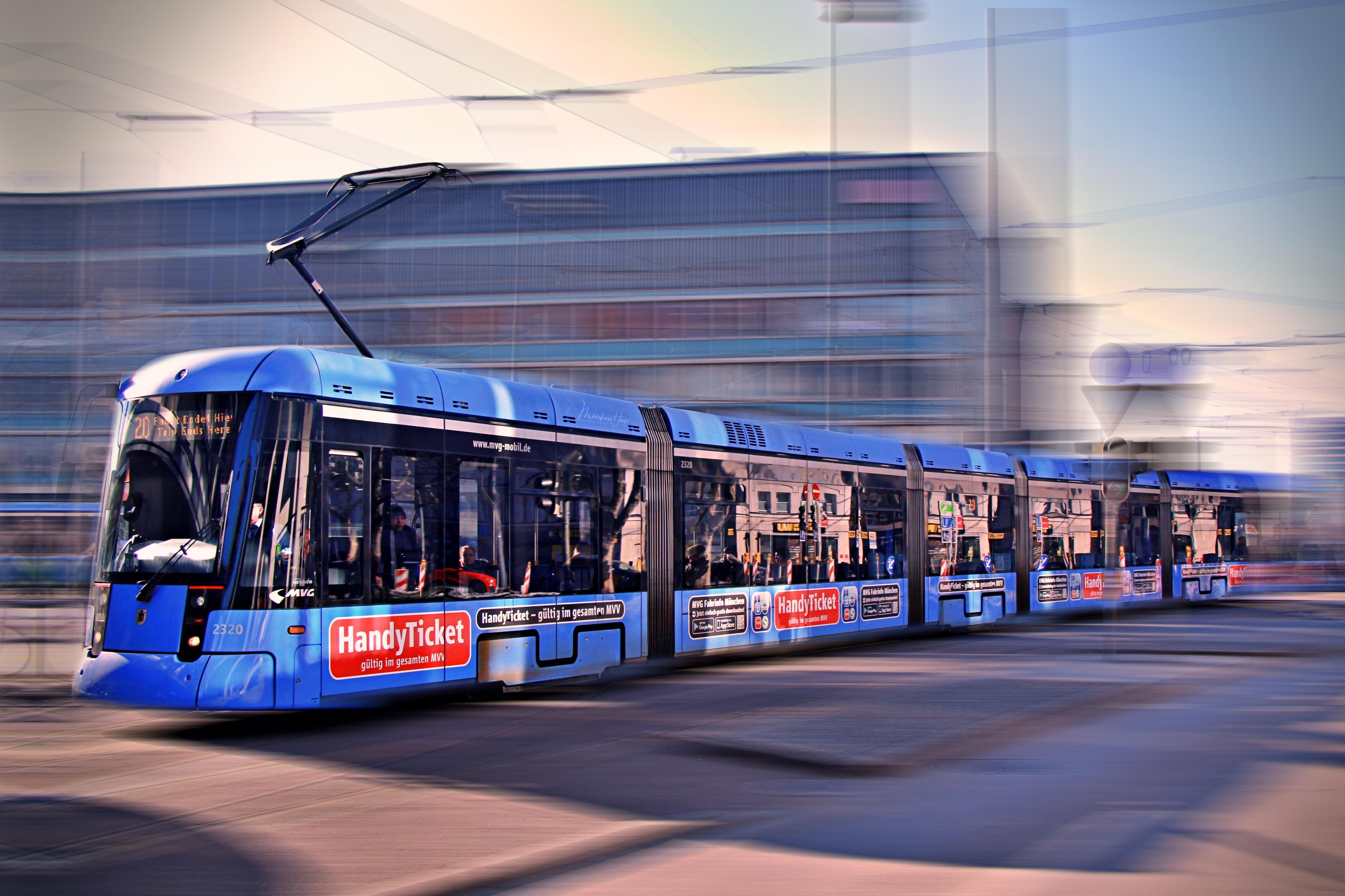 Moderne blaue Straßenbahn der Münchner Verkehrsgesellschaft fährt durch das Stadtgebiet, Hintergrund unscharf durch Bewegung.