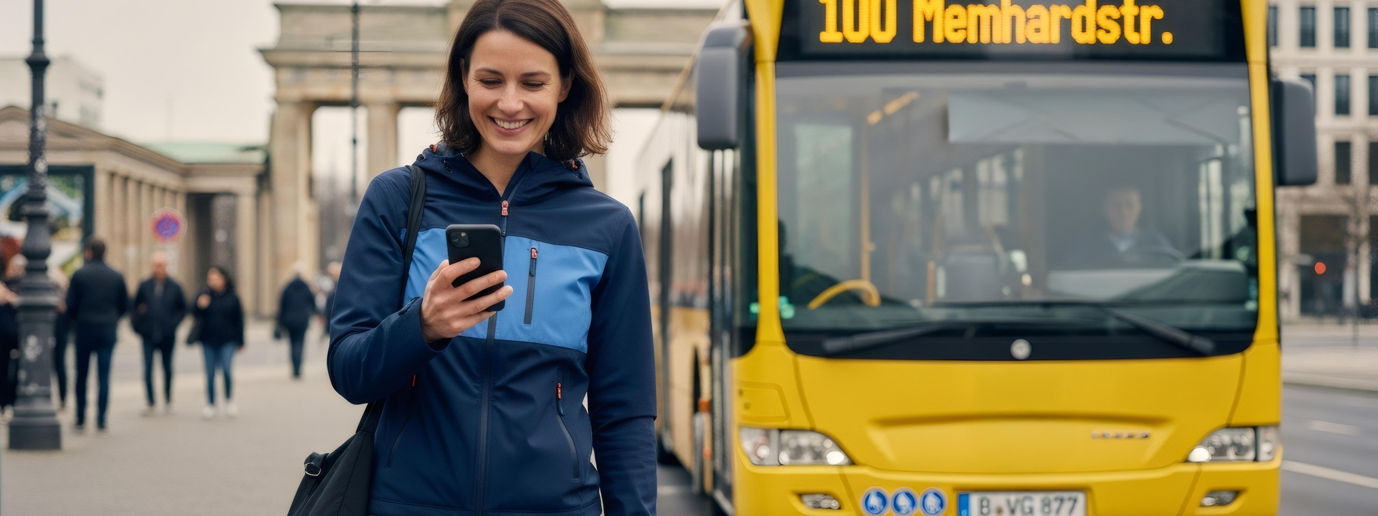 Eine gutgelaunte Frau steht neben einem gelben Bus vor dem Brandenburger Tor.