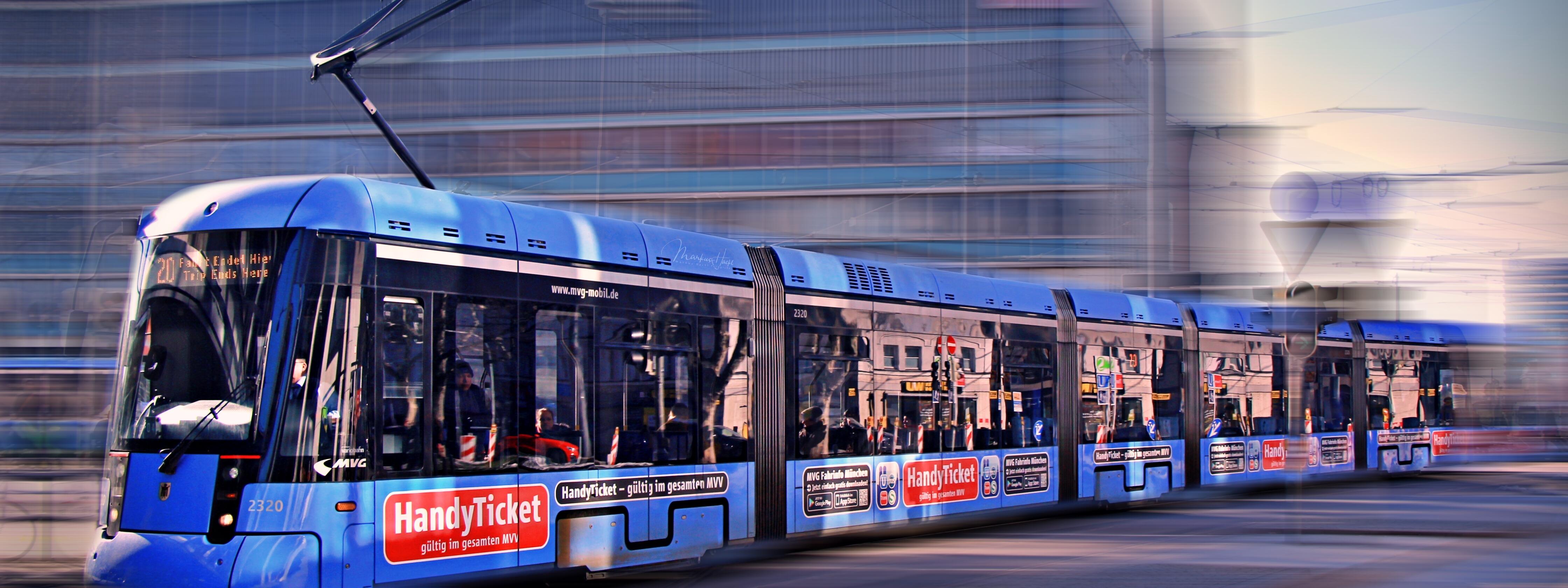 Moderne blaue Straßenbahn der Münchner Verkehrsgesellschaft fährt durch das Stadtgebiet, Hintergrund unscharf durch Bewegung.